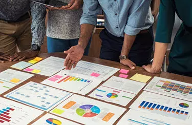 A team of four people reviewing several graphs and charts laid out on a table.